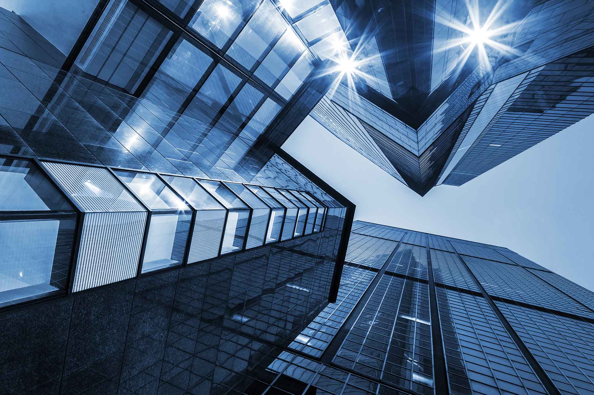 Upward view between modern glass office towers with reflective facades and bright exterior lights. | Haeresis