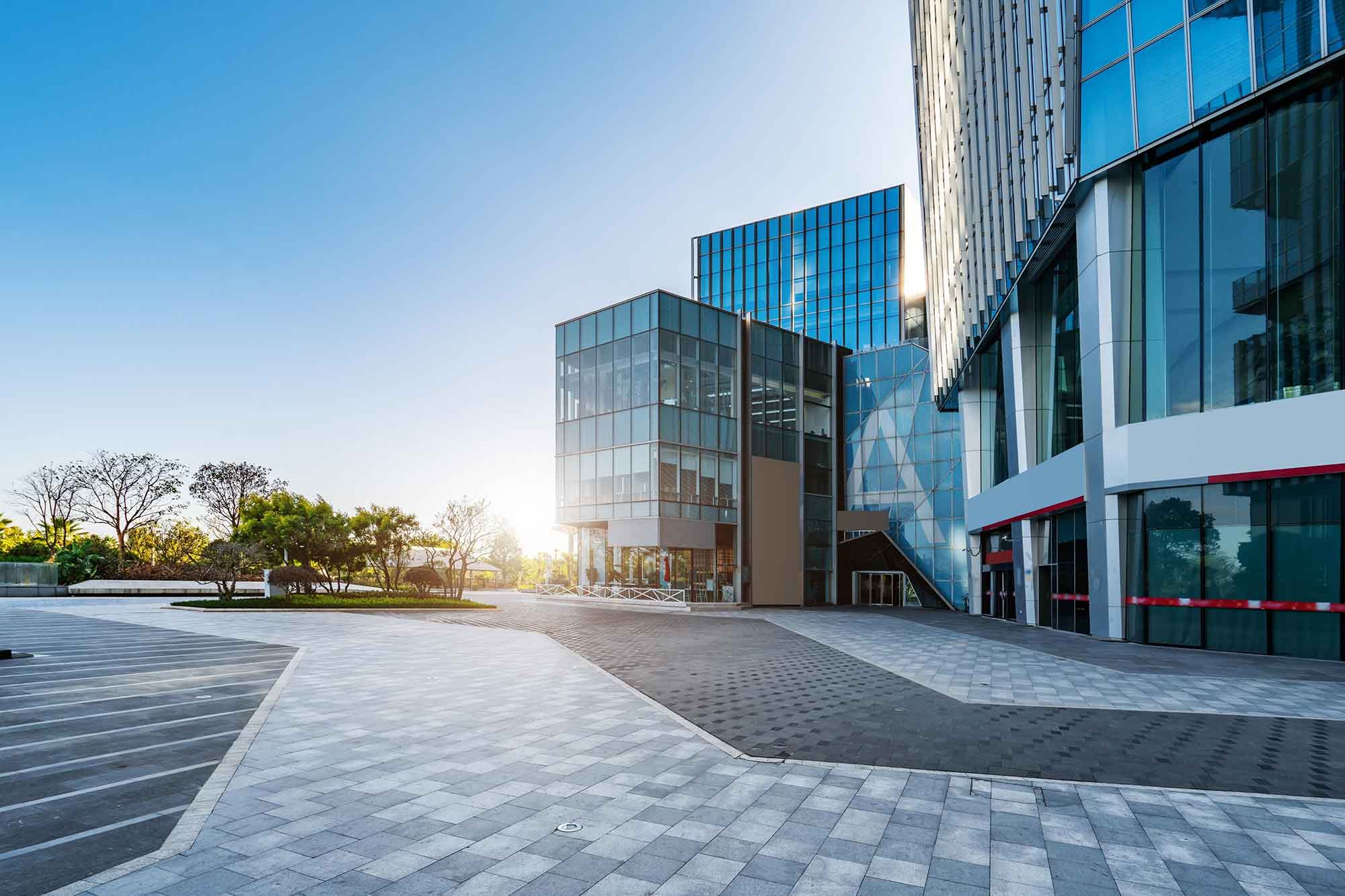 Modern commercial office complex with glass buildings surrounding an open paved plaza. | Haeresis